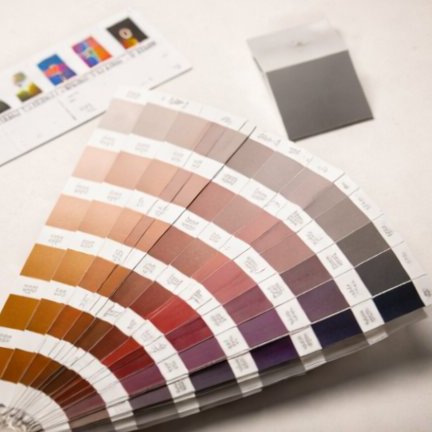A Pantone-style colour fan deck partially fanned open on a cream surface alongside a small printed colour calibration strip.