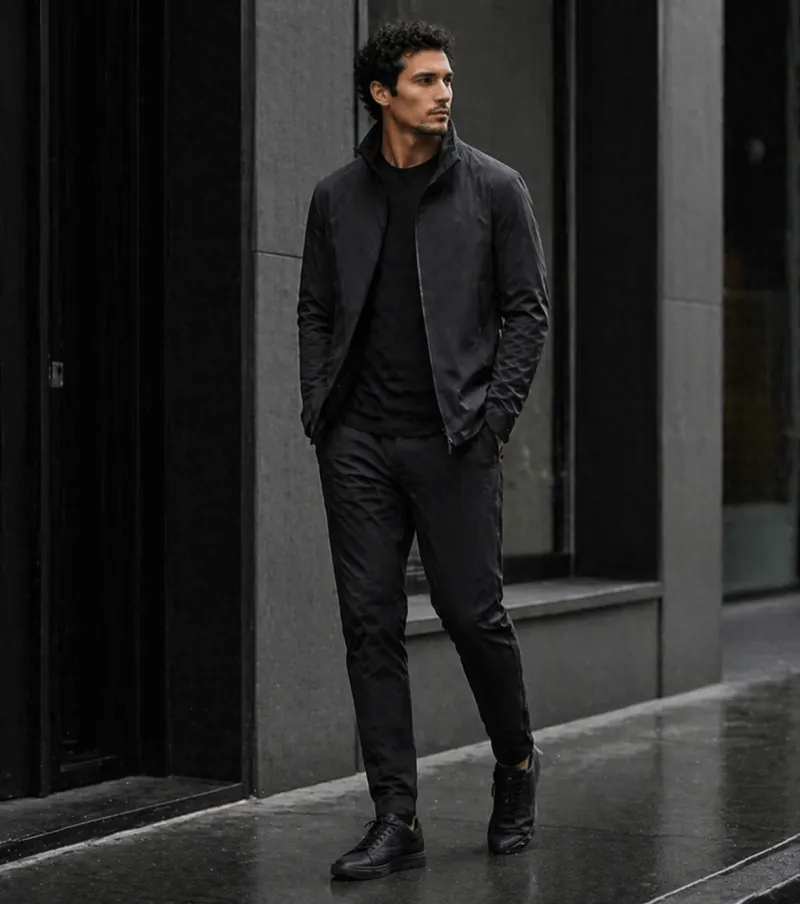 Tech-minimalism: black matte shell jacket, black crewneck, tapered technical trousers, monochrome runners.